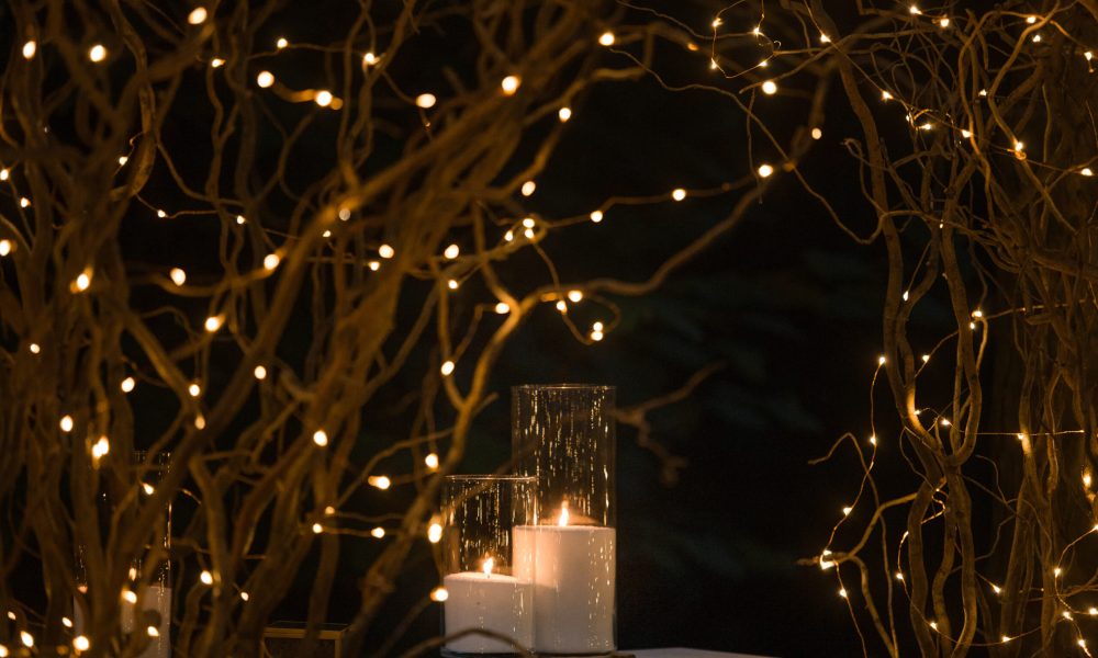 Tall vases with white candles stand under shiny branches